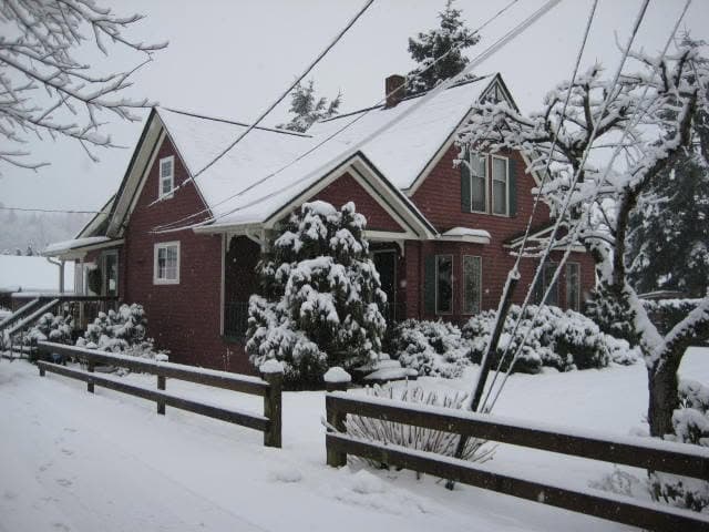 A red gabled house with white trim and a covered porch under snow, behind a split-rail fence, on the Cobweb Antiques property